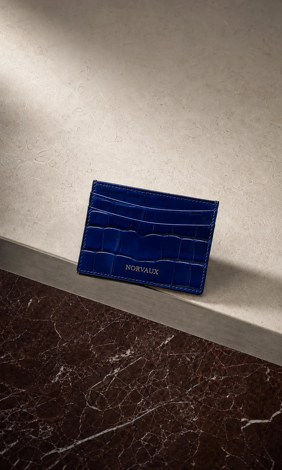 CROVÉ Ocean blue calf leather cardholder arranged on burgundy marble and brushed metal