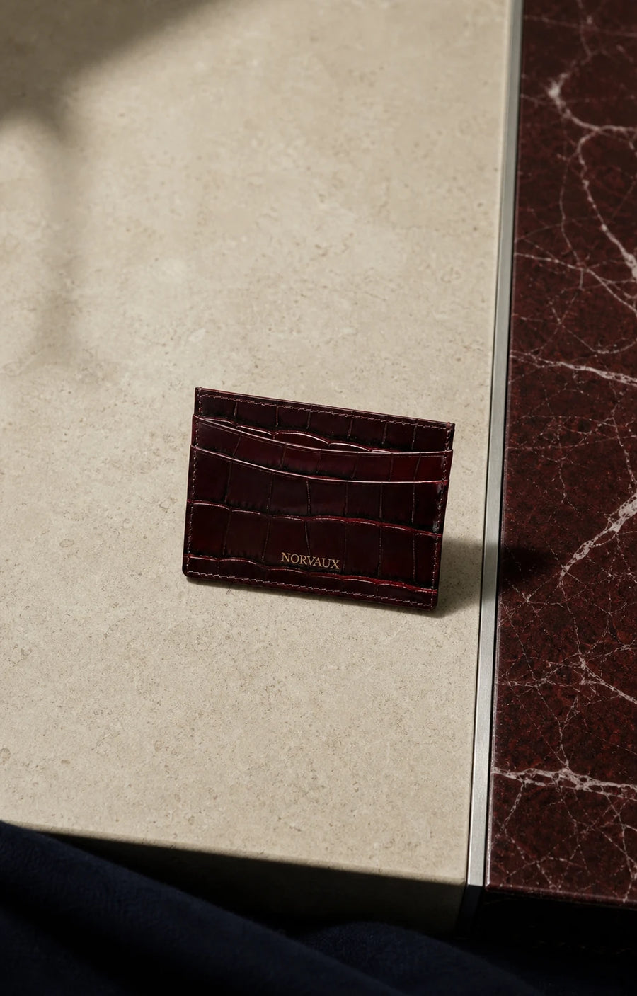 CROVÉ Rubis red calf leather cardholder arranged on pale stone and brushed metal