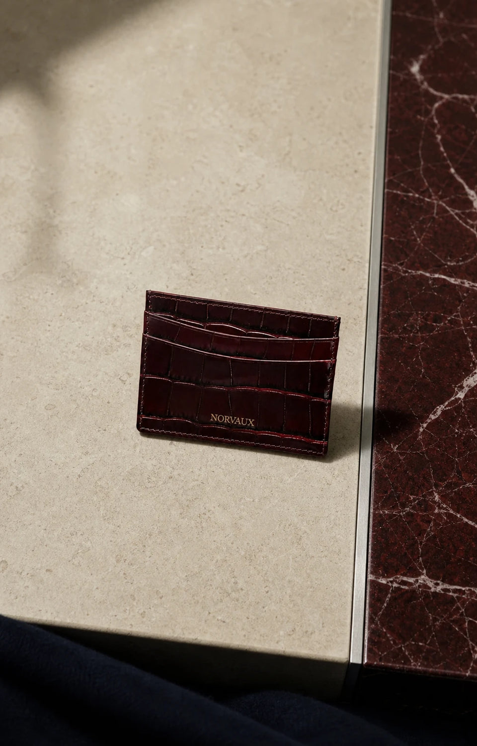 CROVÉ Rubis red calf leather cardholder arranged on pale stone and brushed metal