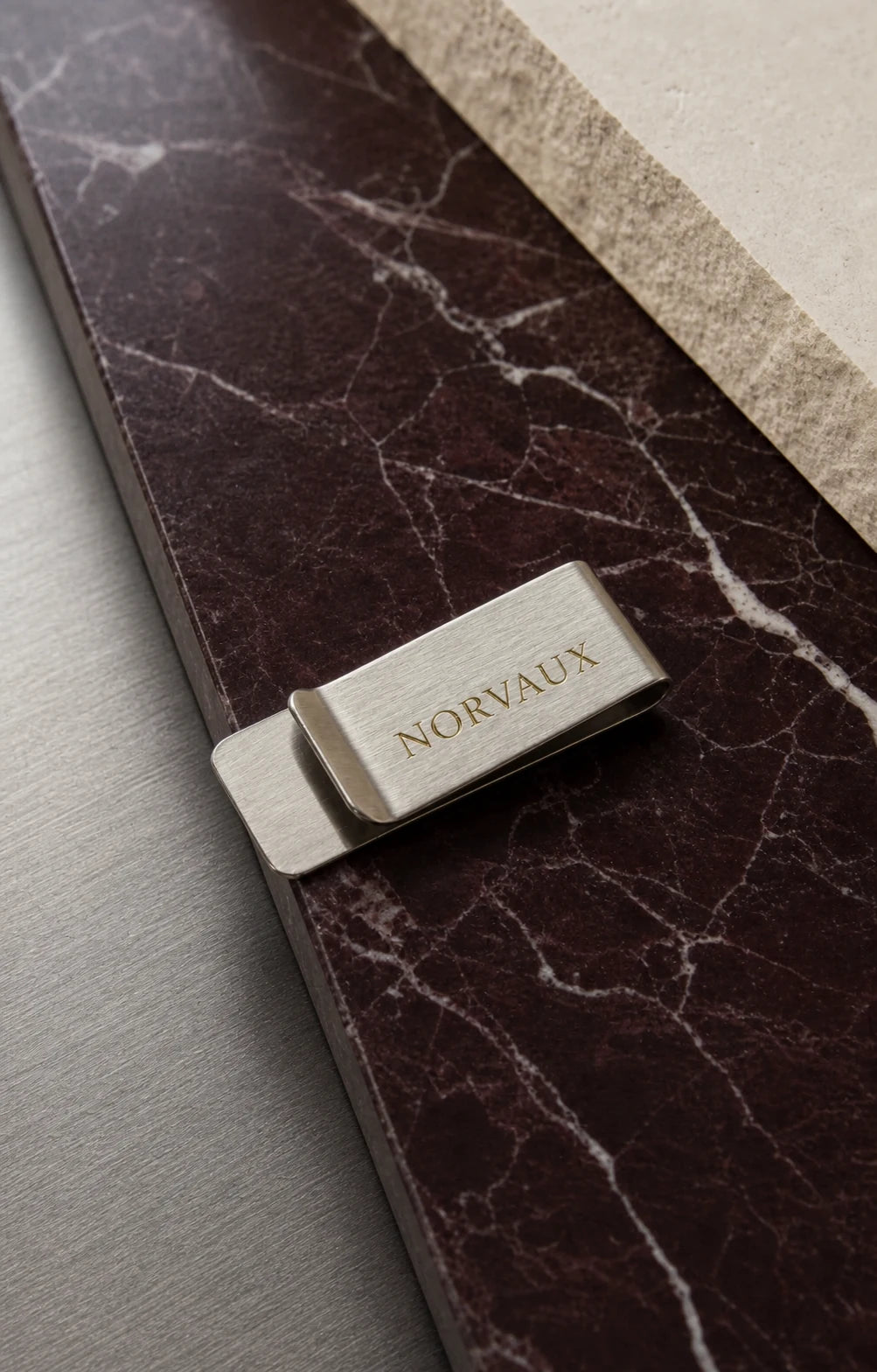 Brushed silver NORVAUX money clip arranged on dark marble