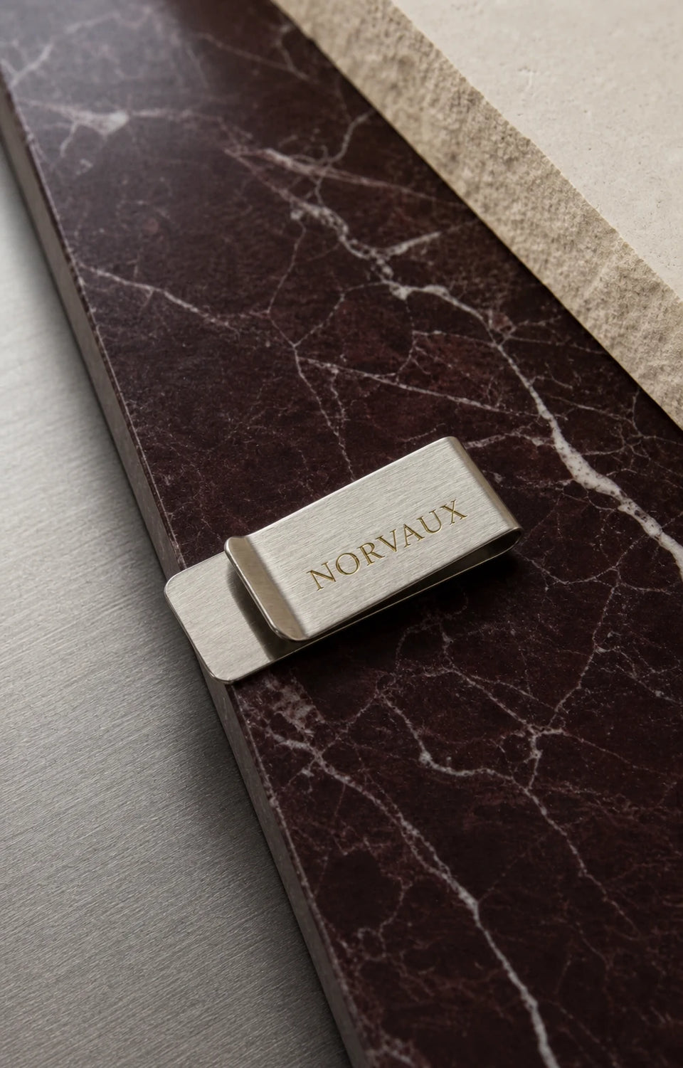 Brushed silver NORVAUX money clip arranged on dark marble
